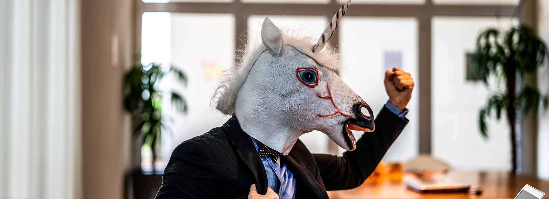 In an office, a man wearing a suit pumps his fist in the air
