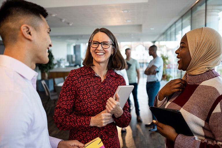 Three coworkers have a friendly discussion while standing in an open-plan office space